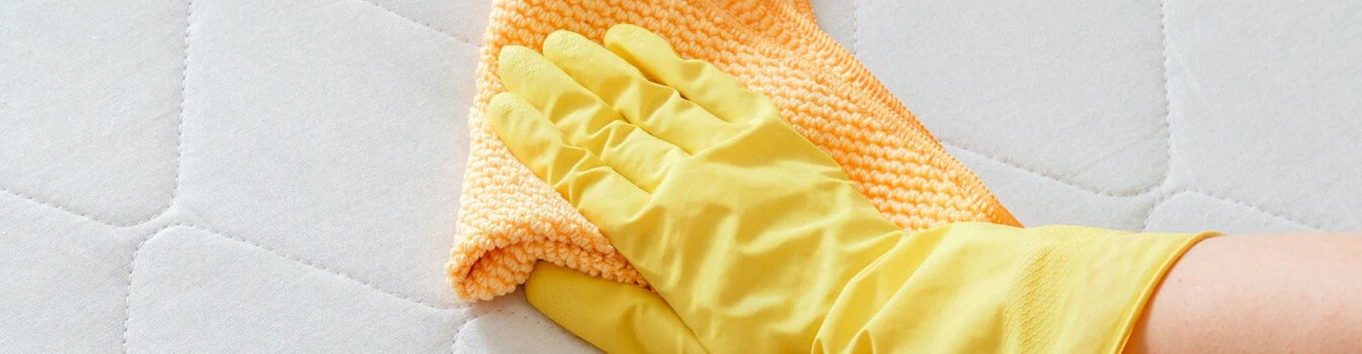 Gloved hand cleaning a mattress with a microfiber cloth, representing Adiwarna Industries’ range of household cleaning and disinfectant products.